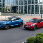 Un SUV Volvo XC40 bleu et une Mini Cooper rouge garés sur une rue moderne, près d'un passage piéton en ville.