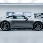 Un expert en costume examine une Porsche grise dans un garage automobile moderne et lumineux.