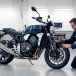 Un mécanicien en combinaison bleue inspecte la roue avant d'une moto bleue dans un atelier professionnel.