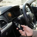 Une main utilise un outil de diagnostic OBD pour vérifier un voyant moteur allumé sur le tableau de bord d'une voiture.