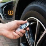 Une main vérifie la pression d'un pneu de voiture avec un manomètre numérique, avec le voyant TPMS visible sur le tableau de bord.