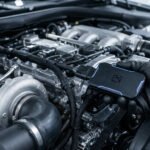 Main gantée installant un boîtier électronique sur un moteur diesel de voiture dans un garage.