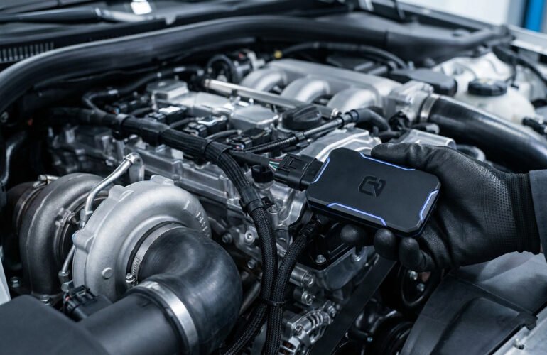 Main gantée installant un boîtier électronique sur un moteur diesel de voiture dans un garage.