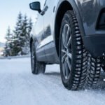 Gros plan sur une voiture roulant sur une route enneigée avec des pneus hiver spécialisés pour une meilleure adhérence.