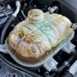 Réservoir de liquide de refroidissement automobile contenant un mélange trouble d'huile marron et de liquide vert.