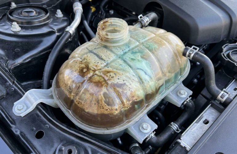 Réservoir de liquide de refroidissement automobile contenant un mélange trouble d'huile marron et de liquide vert.
